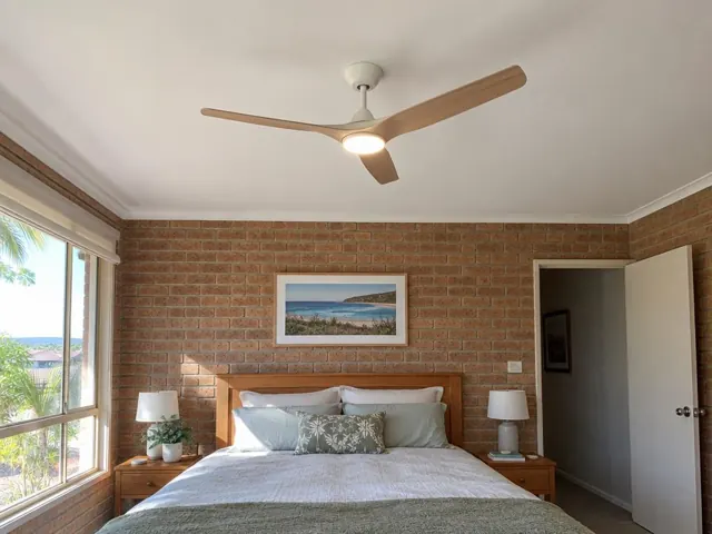 Bedroom with timber ceiling fan above a brick feature wall and bed in Avoca Beach