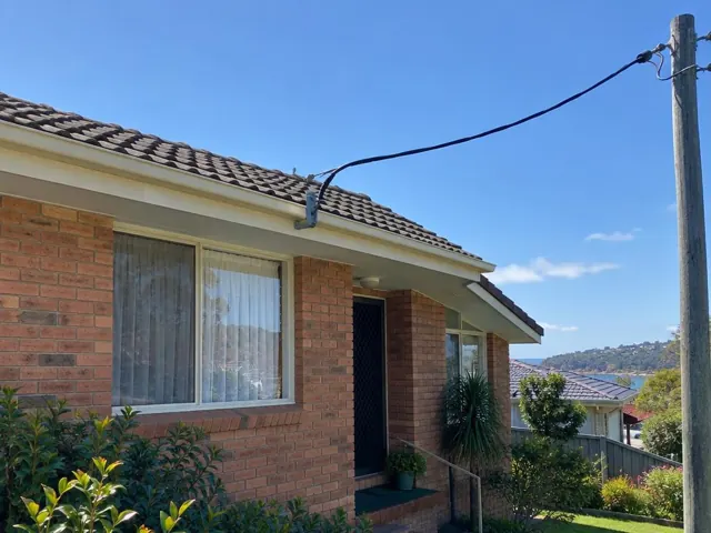 Brick house facade with overhead service cable and attachment bracket near the roofline in Terrigal