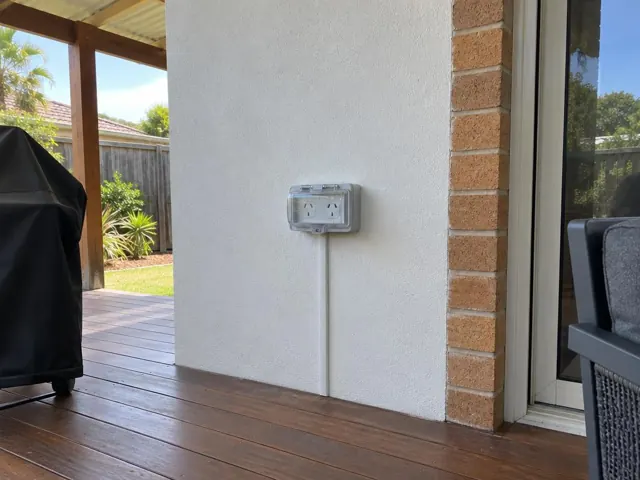 Outdoor double power point on rendered wall beside brick trim and deck in Avoca Beach